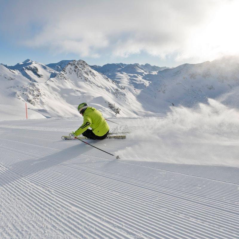 Skier in bright green jacket carving downhill on groomed alpine slope